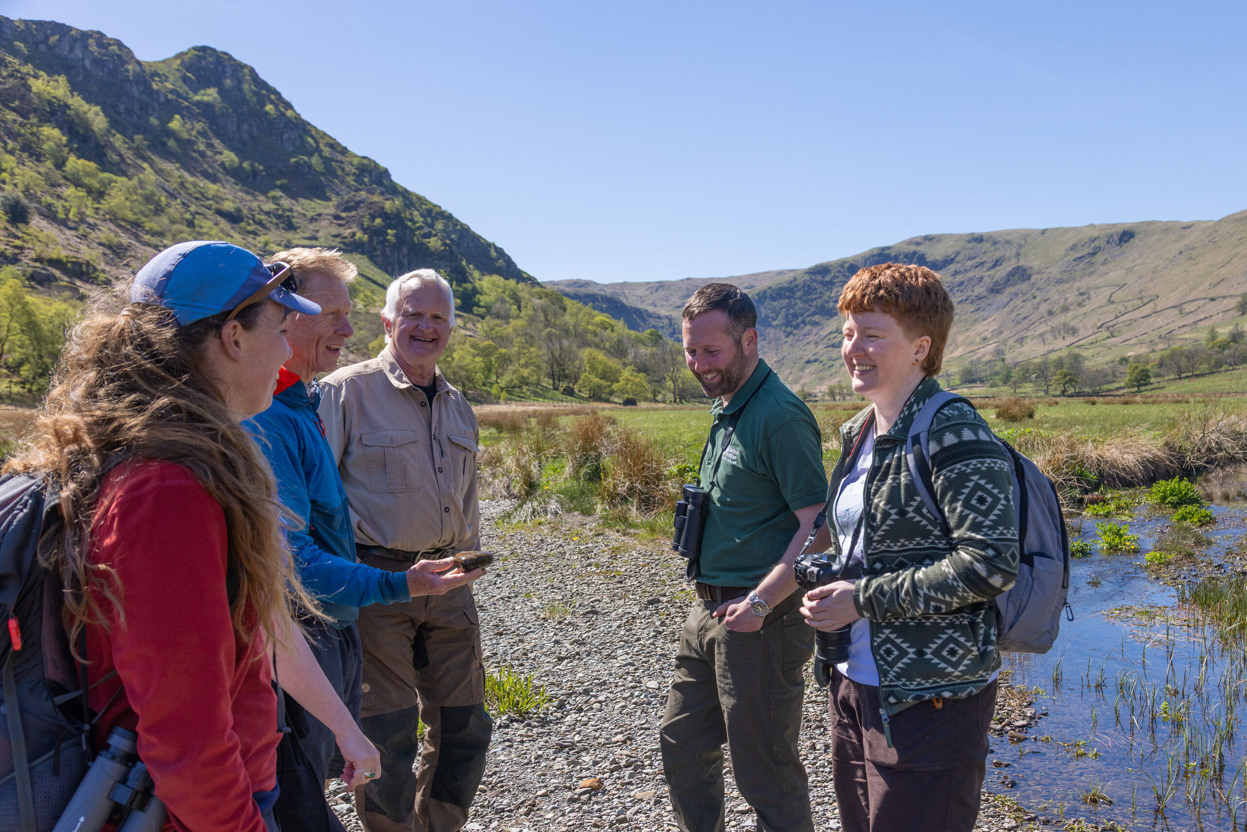 Group of people stood beside a river talking and smiling.