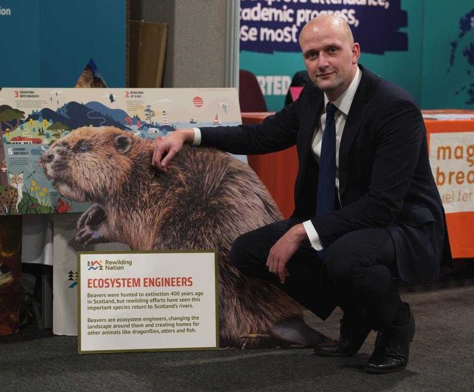 SNP leader Stephen Flynn crouched down next to beaver cut out at a political party conference.