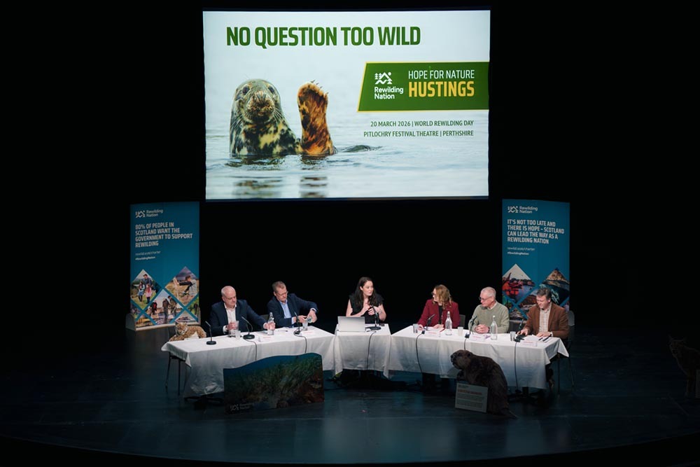 Stage with politicians above sign saying no question too wild at hustings event