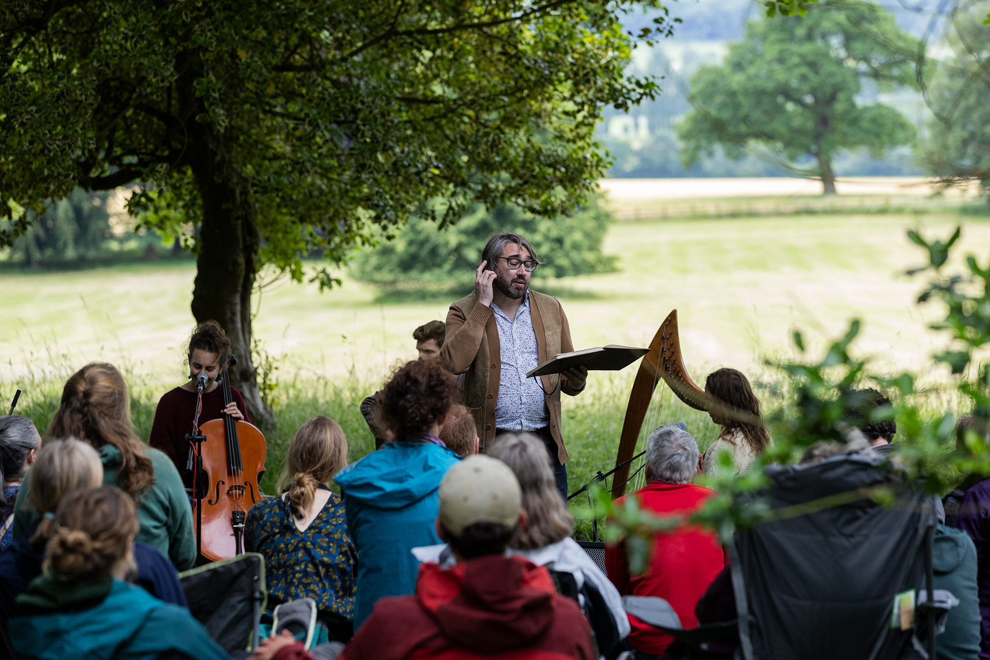 People sat in a field gathered around a group of musicians at Yorkshire Rewilding Network's Rewilding Festival