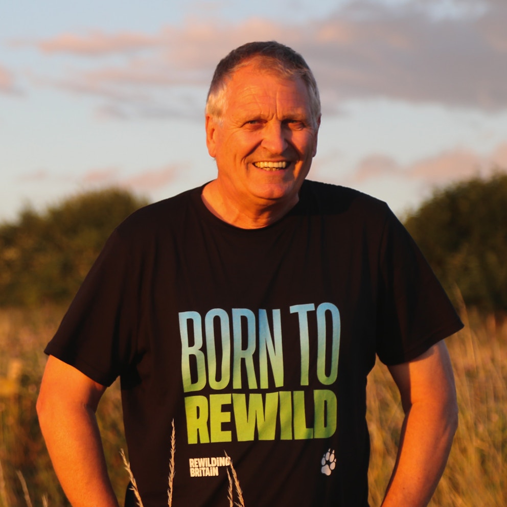 Alastair driver standing confidently in a field wearing a black Rewilding Britain merchandise t-shirt featuring the slogan "Born to Rewild"