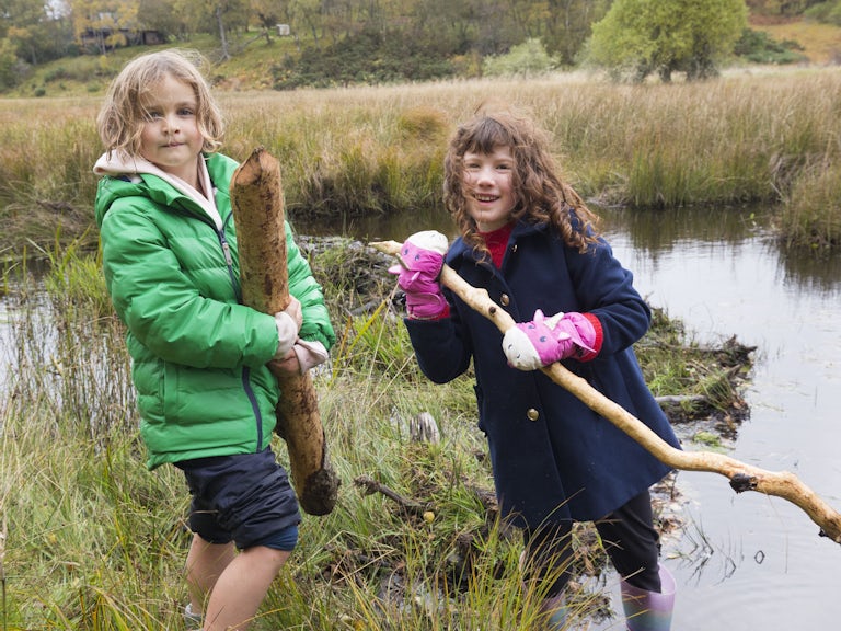 Two children holding beaver gnawed sticks at a gathering of the local community for a ‘beaver day’, organised by Northwoods partner, The Abriachan Forest Trust. Hosted by South Clunes Farm, near Inverness.