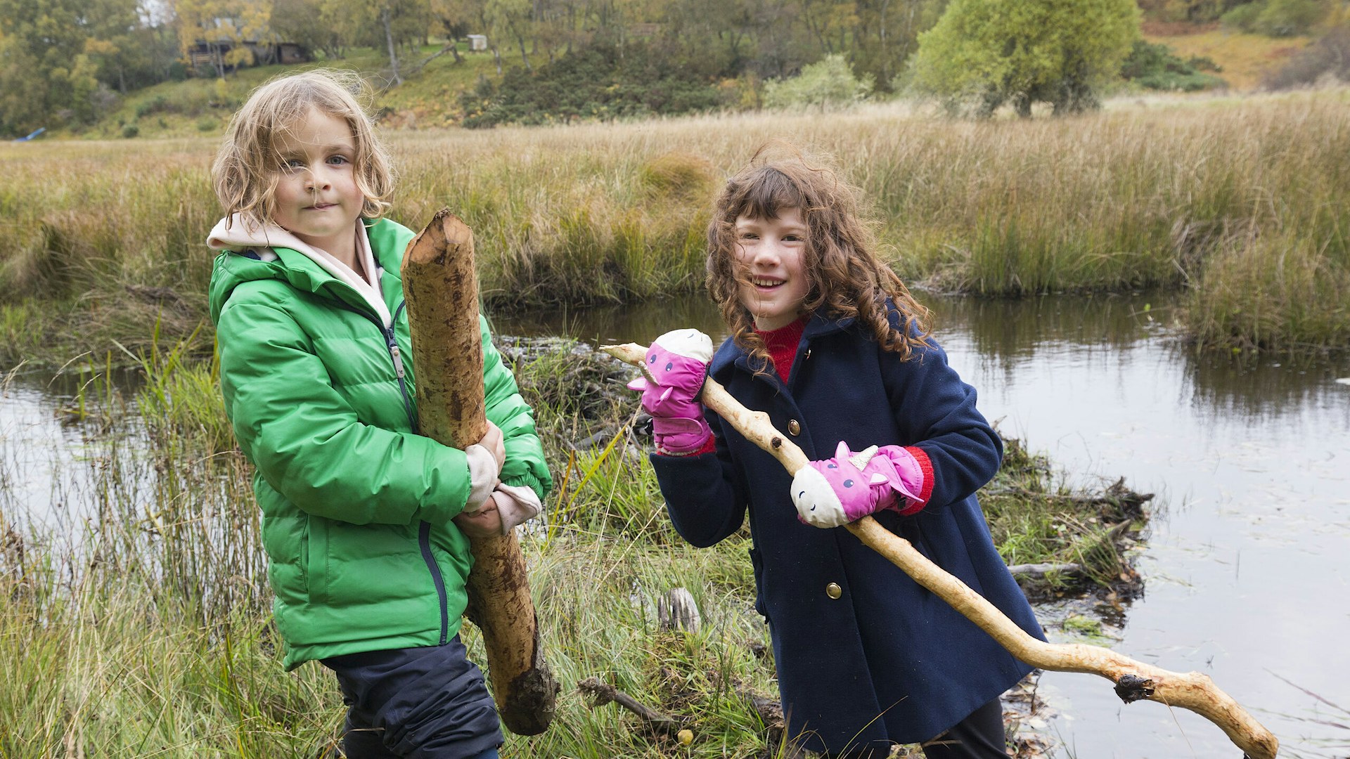 Children in front of a stream holding beaver chewed sticks.