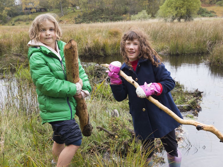 Children in front of a stream holding beaver chewed sticks.