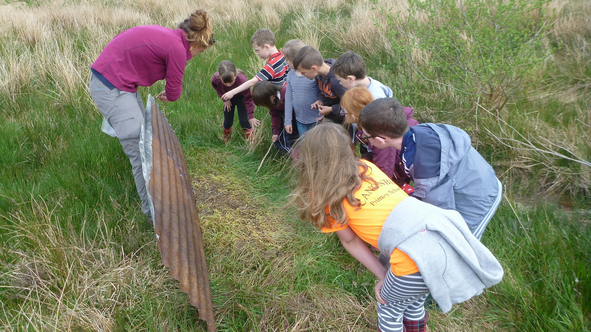 Children crouch to listen to speaker at Tarras Valley, Langholm