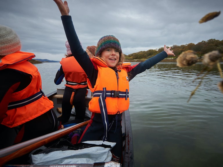 Four volunteers for Seawilding in a small boat releasing oysters in the water