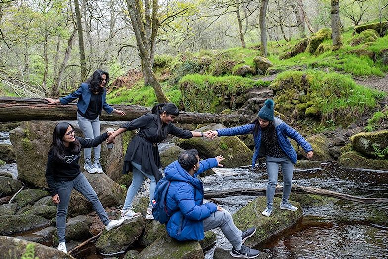 Family of five holding hands and enjoying stepping stones, Peak District