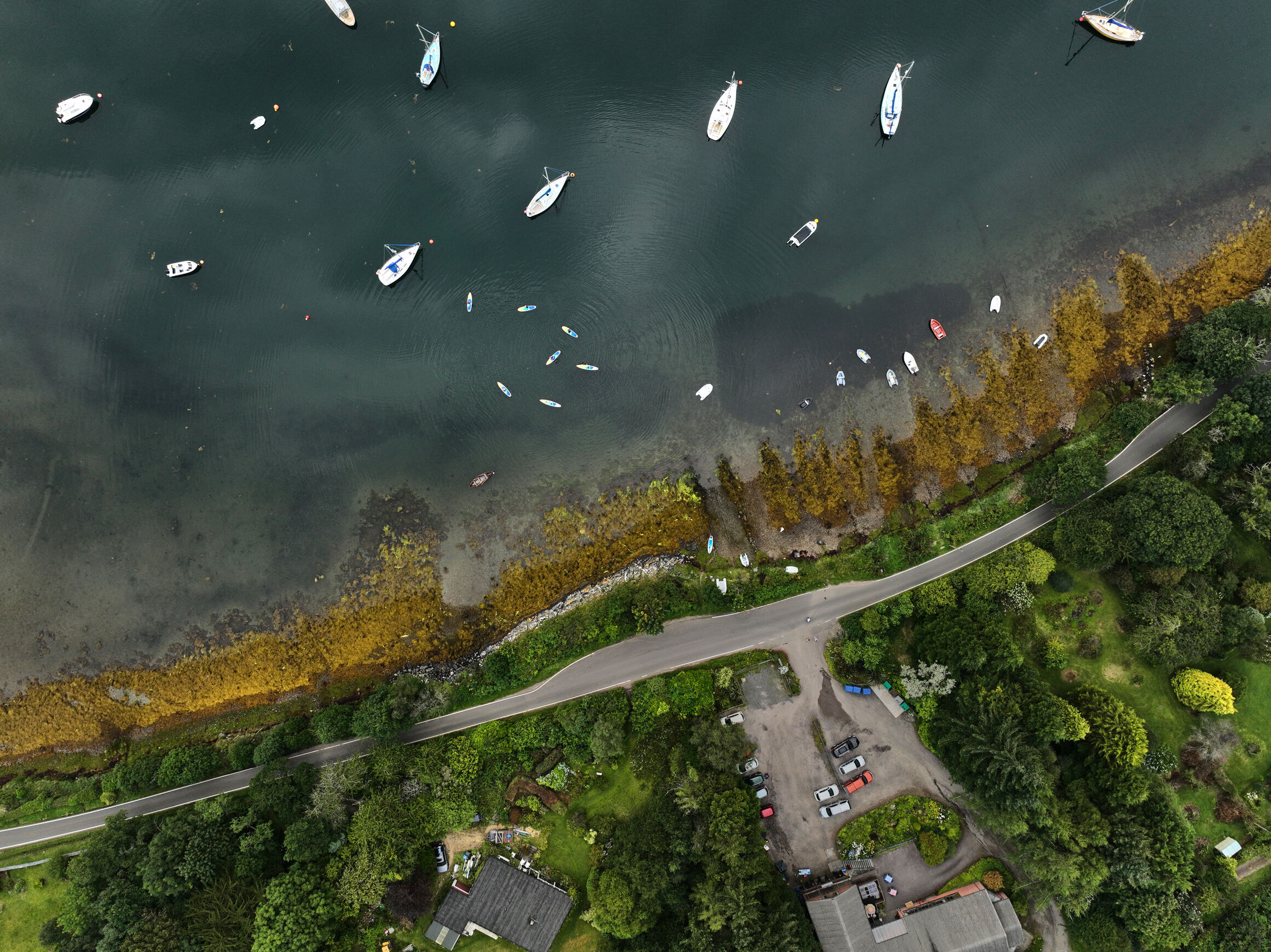 Aerial image of a coast, showing a road, buildings and small boats near the beach.