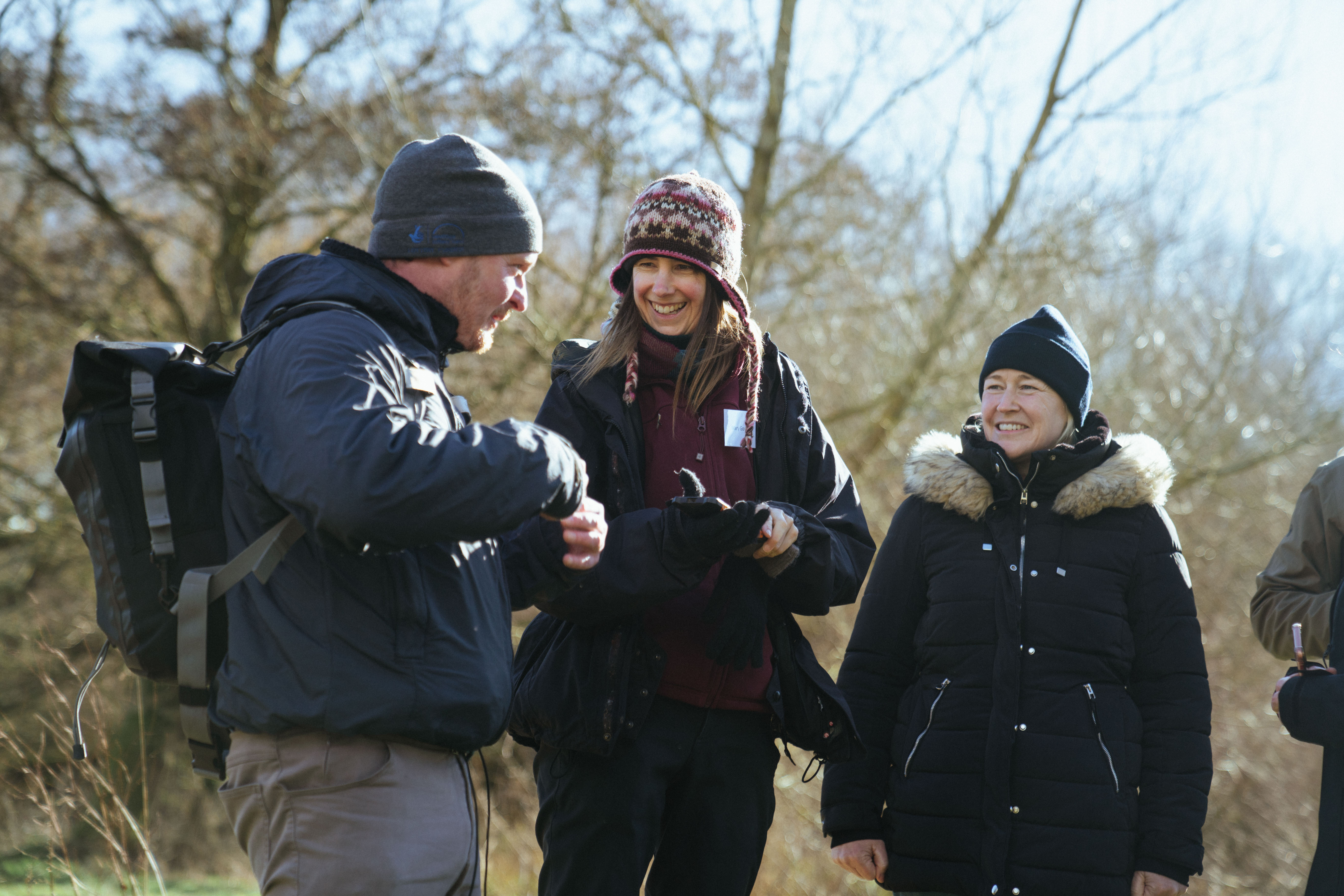 Three people stood in a field chatting and smiling.