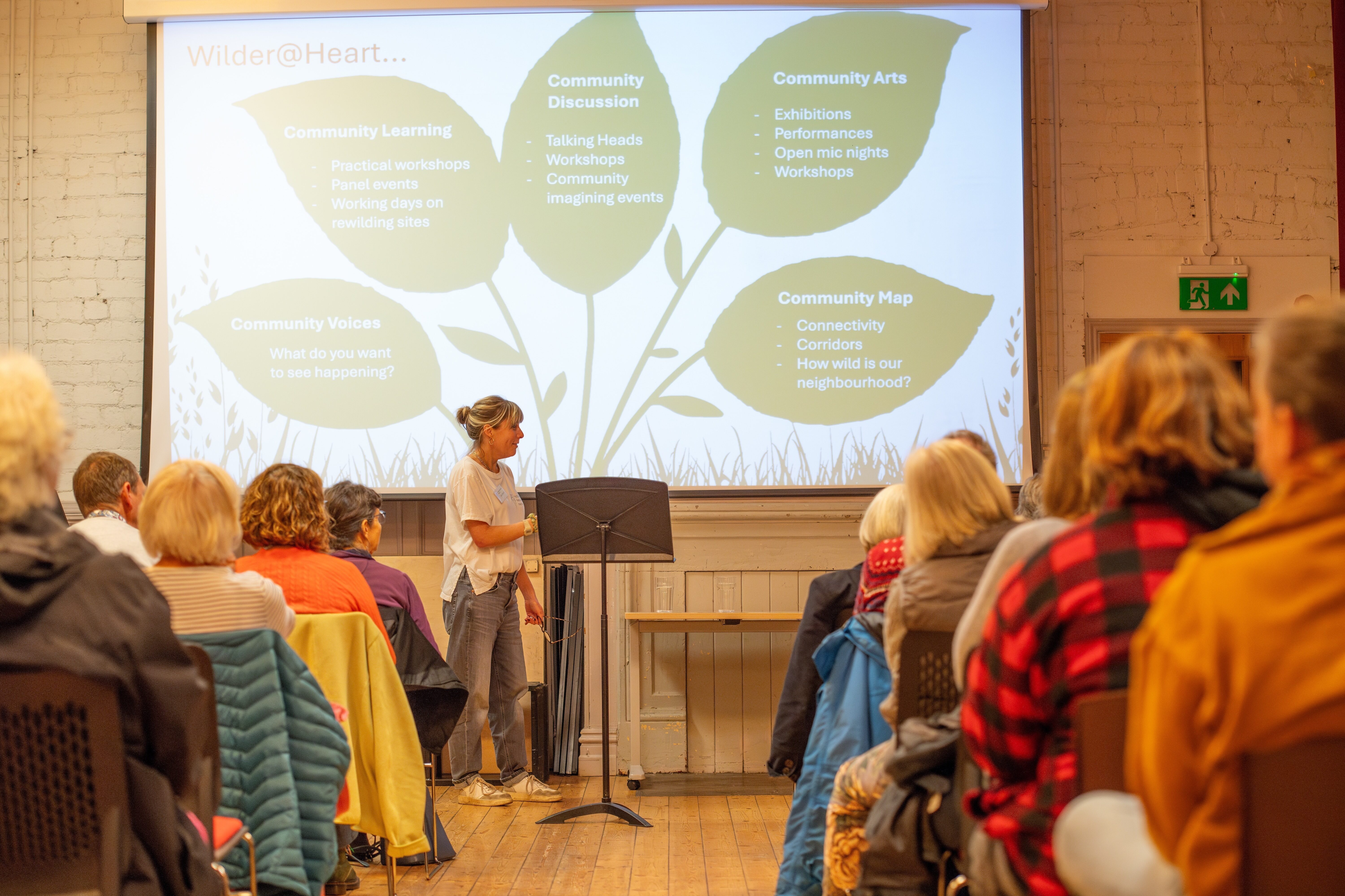 People sat listening to a presentation which is projected on a big screen.