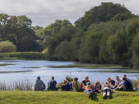 Group of young people from the Youth Rewilding Network sitting near a lake, Knepp.